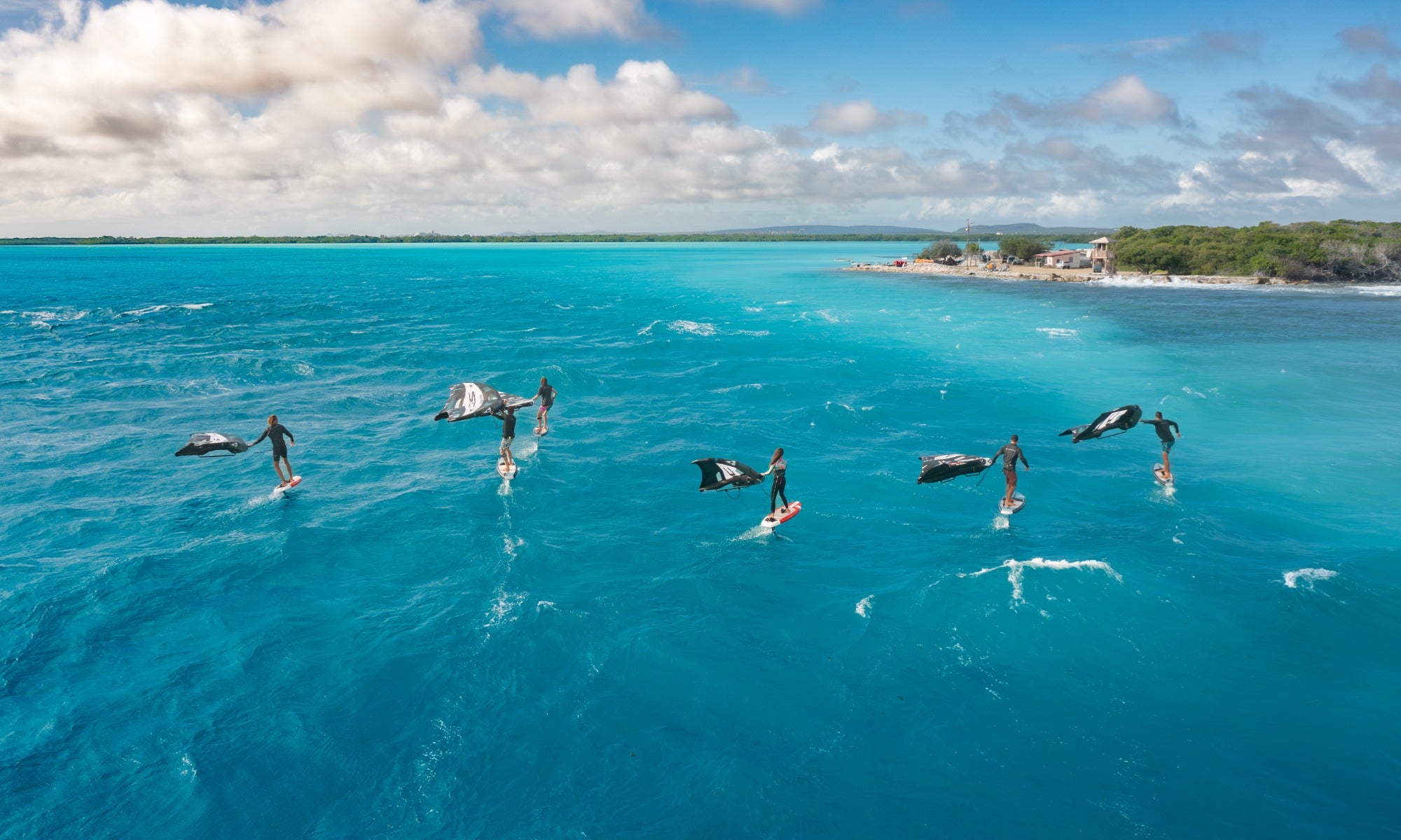 Aerial shot of a dynamic wingfoiling session on SIC Maui foil boards in vibrant blue ocean water.