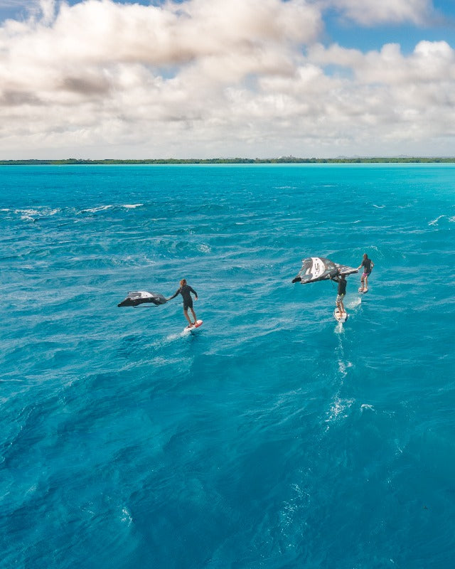 People wingfoiling and diving in a clear blue ocean with a coastal background 