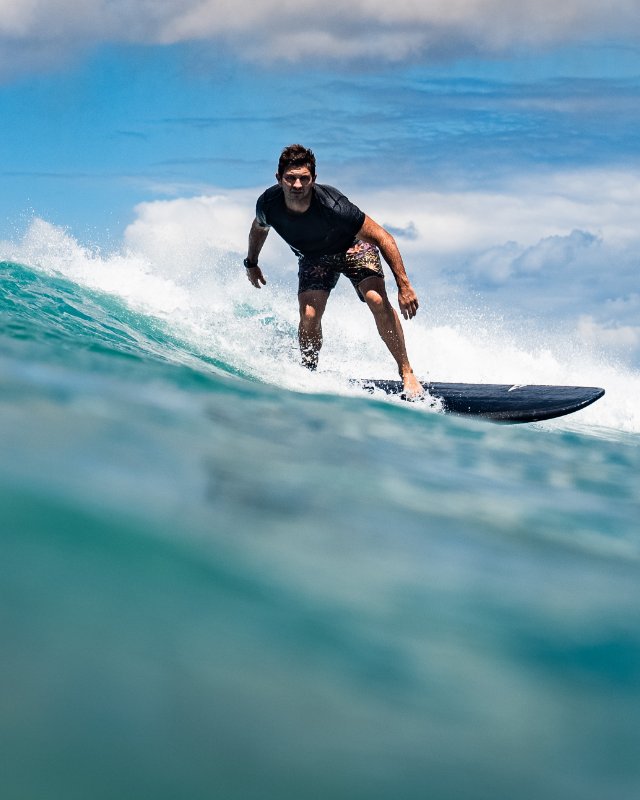 Person surfing on a wave with a clear sky and ocean background with his SIC MAUI Phantom surfboard